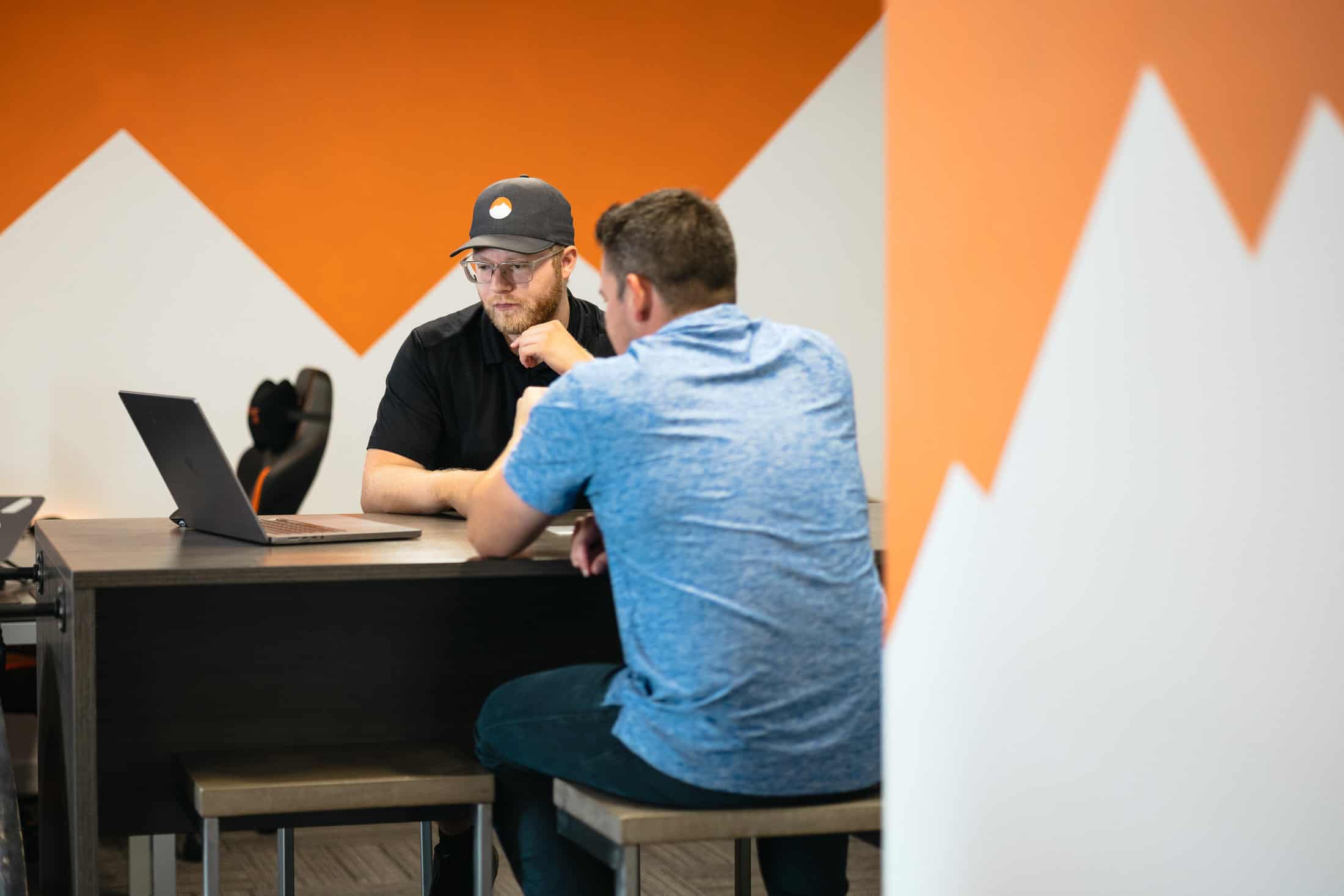 Two men sitting at a table in an office with mountains on the wall.